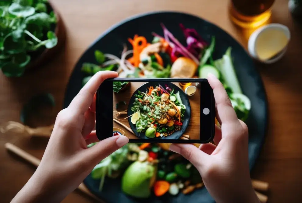 Eine weibliche Bloggerin fotografiert eine Schüssel asiatisches Essen mit ihrem Smartphone. Generative KI.